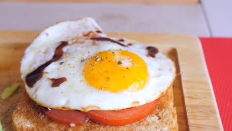 Huevo-Estrellado-Sobre-Una-Tostada-De-Pan-Con-Rodajas-De-Tomate,-Condimentos-Y-Salsa-Balsámica