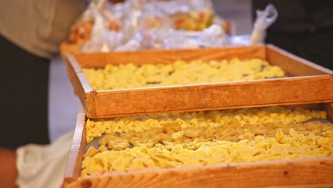 Fresh-handmade-traditional-orecchiettepasta-drying-in-racks-and-trays-on-the-street-of-Bari-Italy-as-women-and-customer-talks-in-the-background,-bright,-warm,-static-shot