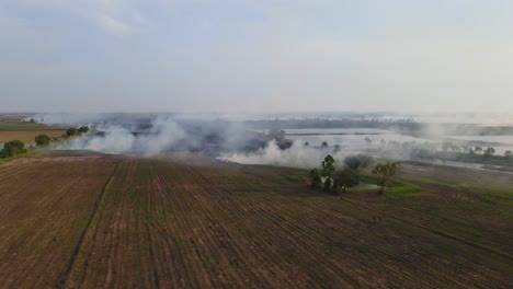 Descending-aerial-footage-revealing-a-newly-tilled-field-and-smoke-rising-from-burning-grass,-Grassland-Burning,-Pak-Pli,-Nakhon-Nayok,-Thailand