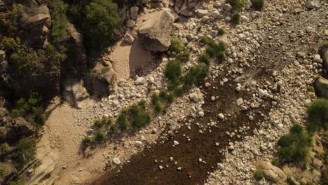 Aerial-top-down-shot-of-person-walking-by-river-rocks-during-sunny-day-in-Argentinian-Landscape