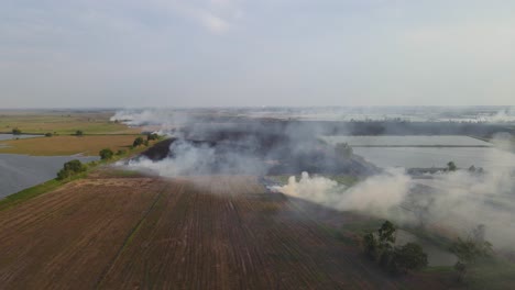 Reverse-aerial-footage-of-this-tilled-farmlands-burning-as-the-farmers-prepare-for-the-planting-season,-Pak-Pli,-Nakhon-Nayok,-Thailand