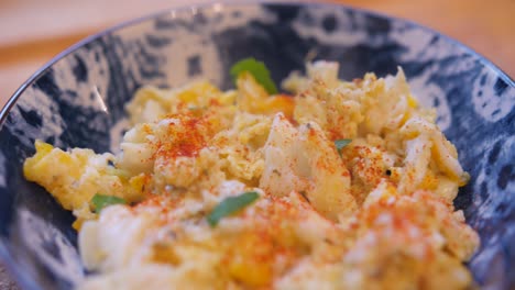 Close-up-view-of-Scrambled-eggs-with-paprika-and-parsley-in-a-blue-bowl-on-a-kitchen-table