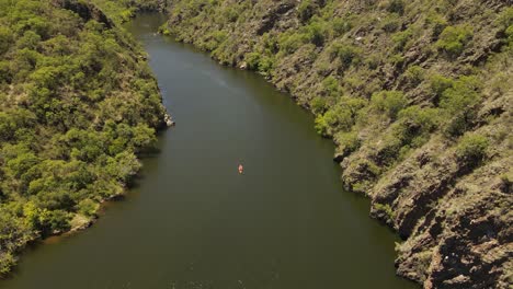 Descending-aerial-top-down-shot-of-orange-kayak-paddling-downwards-the-river-surrounded-by-pure-nature-of-Argentina---Beautiful-sunny-day-in-South-America