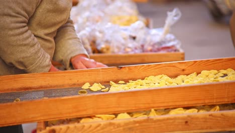 Old-women-making-and-drying-handmade-traditional-orecchiette-pasta,-caring-for-and-tending-to-the-racks-as-she-talks-to-customer,-bright-and-warm,-yellow-pasta-wooden-racks,-static-shot-no-faces
