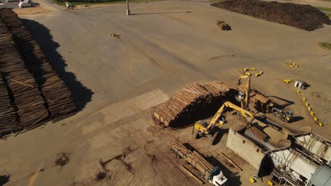 Excavator-lifts-logs-in-paper-mill,-rotating-aerial-view