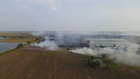 Aerial-footage-sliding-to-the-left-revealing-a-burning-farmland-and-pools-of-water-reverved-for-the-summer,-Grassland-Burning,-Pak-Pli,-Nakhon-Nayok,-Thailand