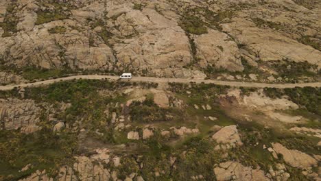 Aerial-tracking-shot-of-white-van-driving-on-rural-road-between-mountains-of-Argentina