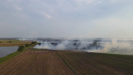 Ascending-aerial-footage-showing-a-pond-on-the-left-and-a-farmland-burning,-Grassland-Burning,-Pak-Pli,-Nakhon-Nayok,-Thailand