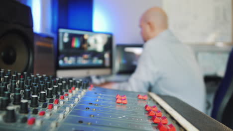 A-man-working-in-a-recording-studio-as-a-video-and-audio-editor-with-mixing-desk-and-computers