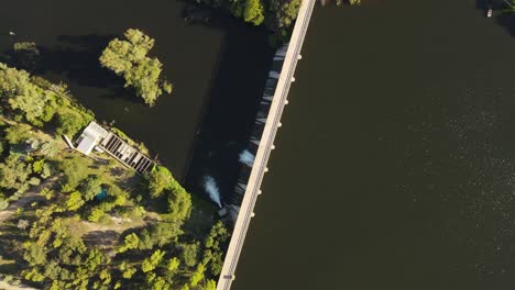 Aerial-top-down-shot-of-water-of-river-dam-reflecting-during-sunlight---Surrounded-by-green-nature-with-treetops-in-Argentina