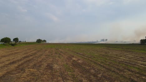 Aerial-footage-just-over-the-tilled-ground-towards-a-burning-farmland-being-prepared-for-planting,-Grassland-Burning,-Pak-Pli,-Nakhon-Nayok,-Thailand