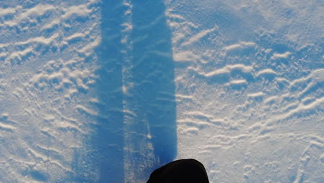 Slowmotion-of-a-person-walking-and-kicking-snow-with-long-shadows-from-the-legs