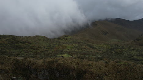 Aerial-View-of-Green-Hills-and-Plateau-Under-Clouds-and-Rucu-Pichincha-Volcano,-Quito,-Ecuador---Drone-Shot