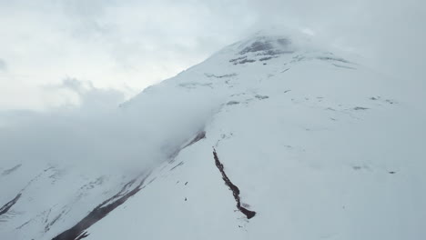 Vista-Aérea-De-Las-Colinas-Del-Volcán-Cotopaxi-Y-El-Glaciar-Bajo-Las-Nubes,-Ecuador