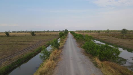 Aerial-footage-over-the-dirt-road-towards-the-horizon-revealing-canals-on-both-sides,-Pak-Pli,-Nakhon-Nayok,-Thailand
