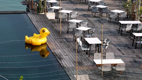 Leuchtend-Gelbe-Gummiente,-Die-Auf-Einem-Swimmingpool-Neben-Tischen-Und-Stühlen-In-Thailand-Schwimmt