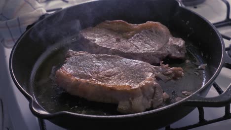 Smoking-steaks-being-halfway-cooked-in-a-cast-iron-skillet-with-oil---slow-motion