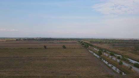 Sliding-aerial-footage-towards-the-right-revealing-a-vast-grassland-and-the-dirt-provincial-farm-road,-Pak-Pli,-Nakhon-Nayok,-Thailand
