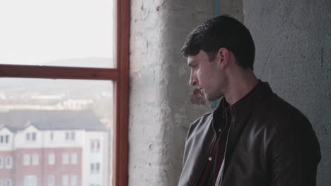 Caucasian-Man-In-Black-Leather-Jacket-Standing-By-The-Studio-Window-Looking-Outside