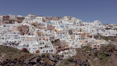 Aerial:-Slow-panning-drone-shot-of-Oia-in-Santorini,-Greece-on-a-sunny-day
