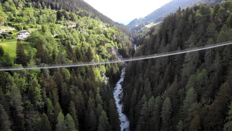 Aerial-flyover-over-the-Goms-suspension-bridge-high-up-above-Rhone-river-valley-in-Valais,-Switzerland-with-a-hiker-standing-on-the-bridge