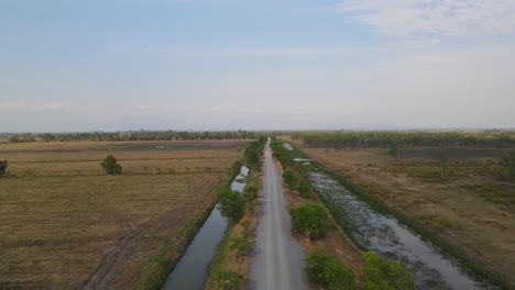 Aerial-ascending-footage-revealing-this-farm-road-with-canals-on-both-sides-and-a-beautiful-horizon,-Pak-Pli,-Nakhon-Nayok,-Thailand