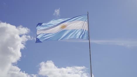 Toma-En-Cámara-Lenta-De-La-Bandera-Argentina-Ondeando-Contra-El-Cielo-Azul-Y-Las-Nubes-Durante-El-Verano---ángulo-Bajo,-4k