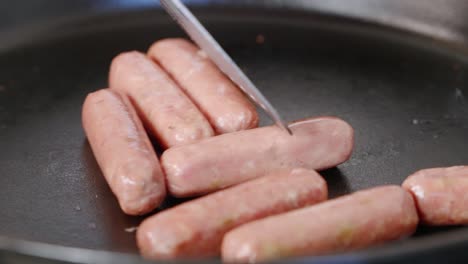 Metal-spatula-turning-and-flipping-breakfast-sausages-in-hot-cast-iron-skillet-with-oil-splatters-and-steam-in-slow-motion