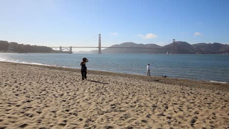 Woman-walking-along-the-shore-in-Crissy-Field-as-an-watches-his-dog