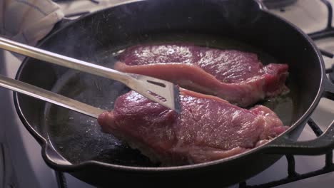 Steaks-being-cooked-and-flipped-in-a-cast-iron-skillet-with-oil---slow-motion