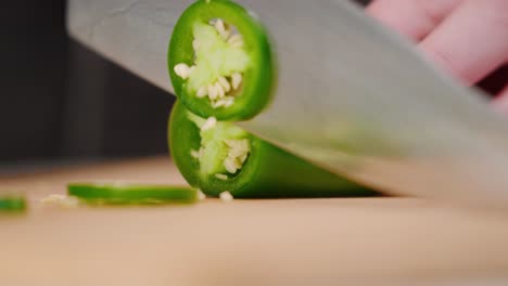 Chefs-hand-cutting-whole-green-jalapeño-pepper-with-sharp-knife-onto-cutting-board-into-pile-of-slices-in-slow-motion