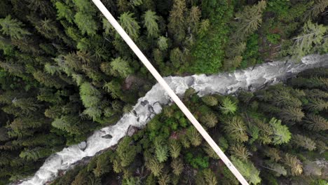 Top-down-aerial-view-of-the-Goms-suspension-bridge-with-a-hiker-walking-across-high-up-above-Rhone-river-valley-in-Valais,-Switzerland