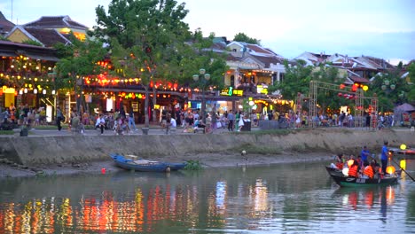Tourists-on-small-boats-with-the-Hoi-An-ancient-town-in-the-background-crowded-with-toursts