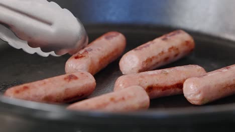 Tongs-flipping-breakfast-sausages-in-hot-cast-iron-pan-to-cook-evenly