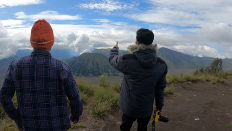 two-tourists-who-walk-while-pointing-to-Mount-Bromo,-after-that-take-pictures-of-the-beauty-of-Mount-Bromo