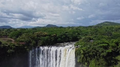 Tilt-down-shot-featuring-a-beautiful-waterfall-in-the-Mexican-jungle-is-surrounded-by-lush-green-vegetation-on-both-sides-with-the-view-of-hills-in-the-background