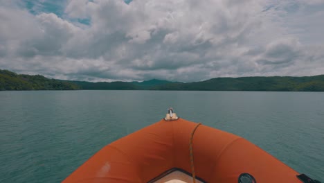 View-from-the-front-of-an-orange-speed-boat-driving-fast-in-the-sea-with-coasts-of-some-island-in-the-background-during-a-cloudy-day