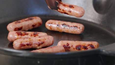 Tongs-reach-into-hot-pan-of-cooked-breakfast-sausages-and-grab-one-with-grill-marks-to-plate