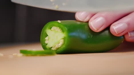 Chef's-hand-cutting-green-jalapeño-pepper-with-sharp-knife-onto-cutting-board-into-pile-of-slices-in-slow-motion