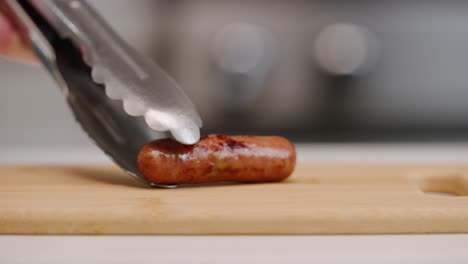 Setting-a-single-sausage-link-down-onto-cutting-board-for-breakfast-with-tongs-in-bright-kitchen-shallow-focus-slow-motion-4k