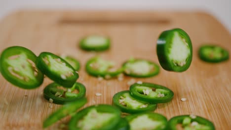 Bright-green-jalapeños-being-dropped-onto-a-wooden-cutting-board,-bouncing-and-falling-in-a-pile