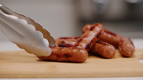 Setting-a-sausage-link-down-on-cutting-board-with-tongs-for-breakfast-in-bright-kitchen-in-slow-motion-4k