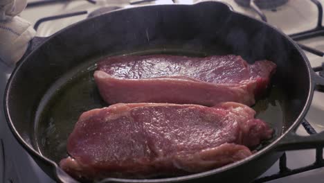 Steaks-being-cooked-in-a-cast-iron-skillet-with-oil---slow-motion