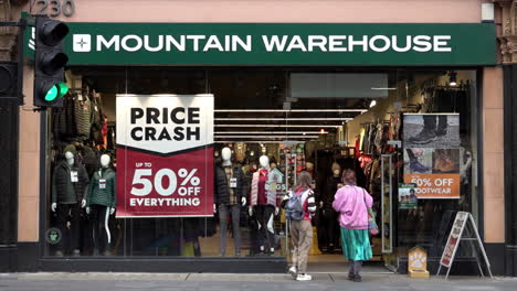 People-walk-into-a-Mountain-Warehouse-shop-advertising-a-“Price-Crash”-sale-in-the-window-on-Tottenham-Court-Road