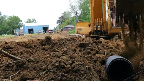 Low-angle-view-of-man-operating-a-yellow-John-Deere-excavator-to-cover-a-drainage-tube-for-a-pond-at-a-new-land-development-site