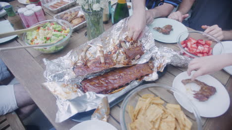 Overhead-View-Of-Hands-Tucking-Into-Cooked-BBQ-Spare-Ribs-On-Table