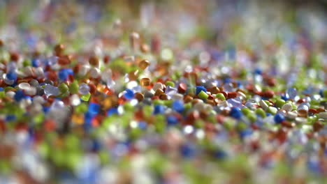 Colored-plastic-pellets-falling-onto-mirror-in-slow-motion