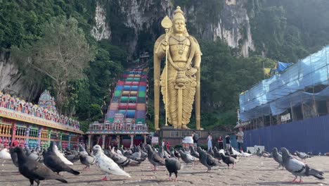 Flock-of-pigeons-walking-and-flying-around-searching-for-food-from-the-floor-at-the-famous-Batu-Caves-Hindu-Temple-in-Selangor,-Kuala-Lumpur,-Malaysia