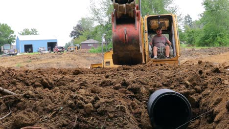 Low-angle-view-of-man-operating-a-yellow-John-Deere-excavator-to-cover-a-drainage-tube-for-a-pond-at-a-new-land-development-site