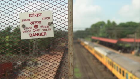 Dolly-shot-to-the-right-of-danger-sign-board-and-AC-train-standing-at-the-station